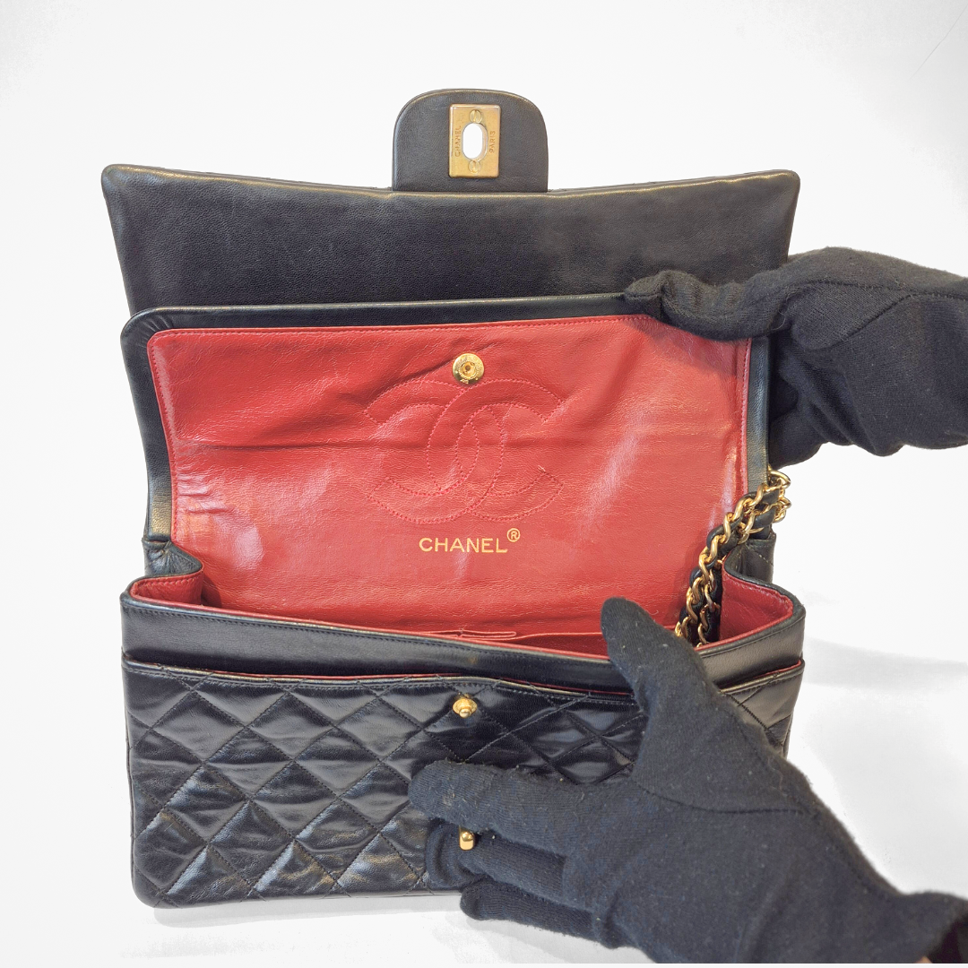 Black Chanel handbag with gold chain handle and clasp on a white background