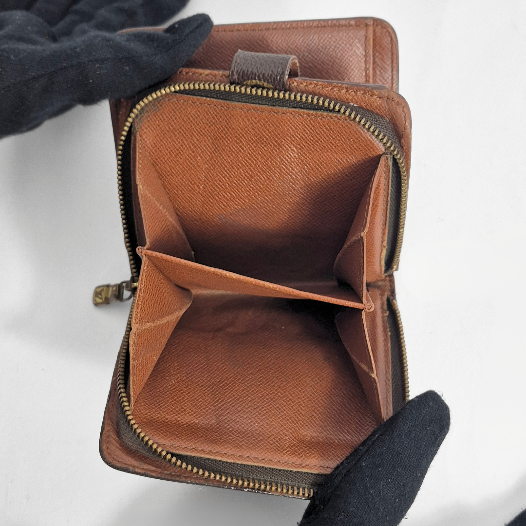 Brown leather wallet with a zipper held open by black gloves on a white background