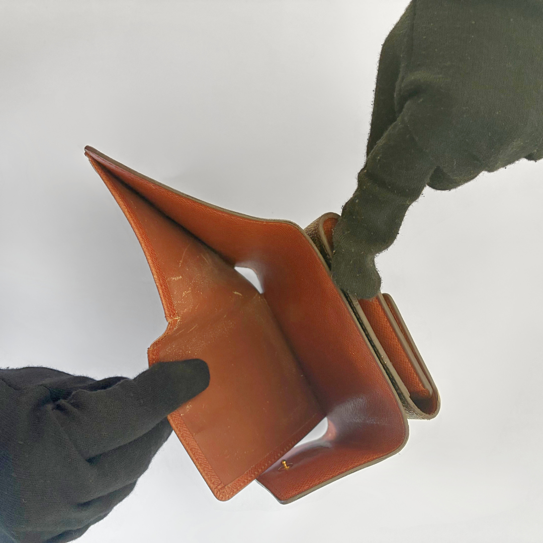 Brown leather wallet held by a gloved hand against a white background