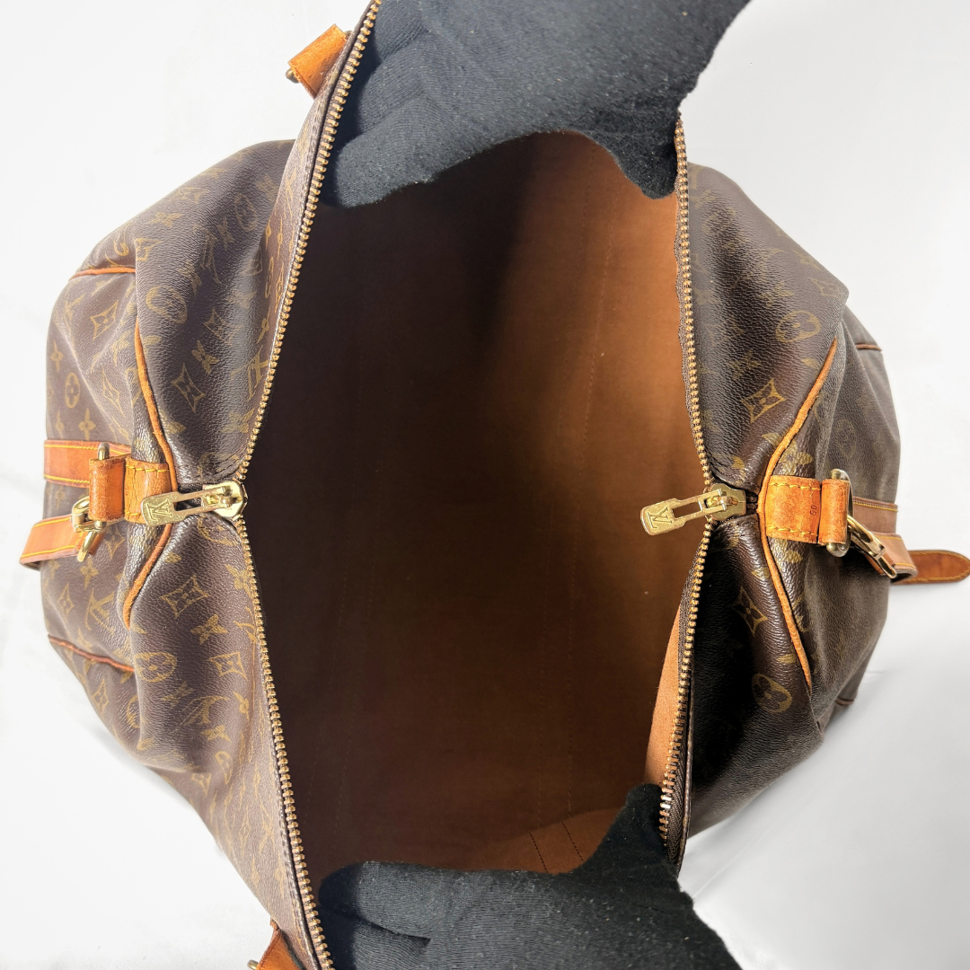 A Louis Vuitton monogram canvas duffel bag shown open from the top, with black gloves holding the opening against a plain white background.