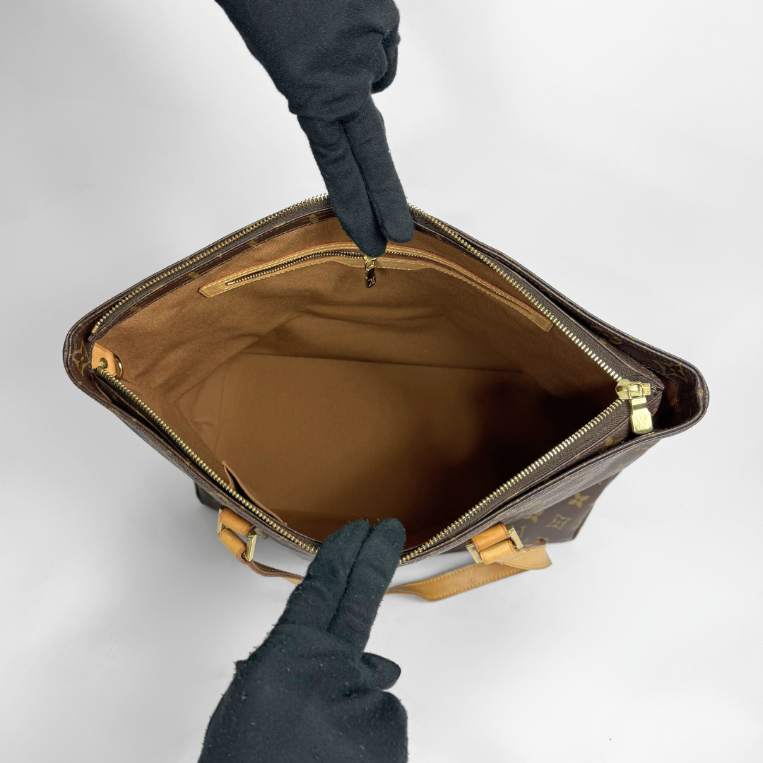 Brown leather bag with gold zipper being held open by gloved hands on a light gray background