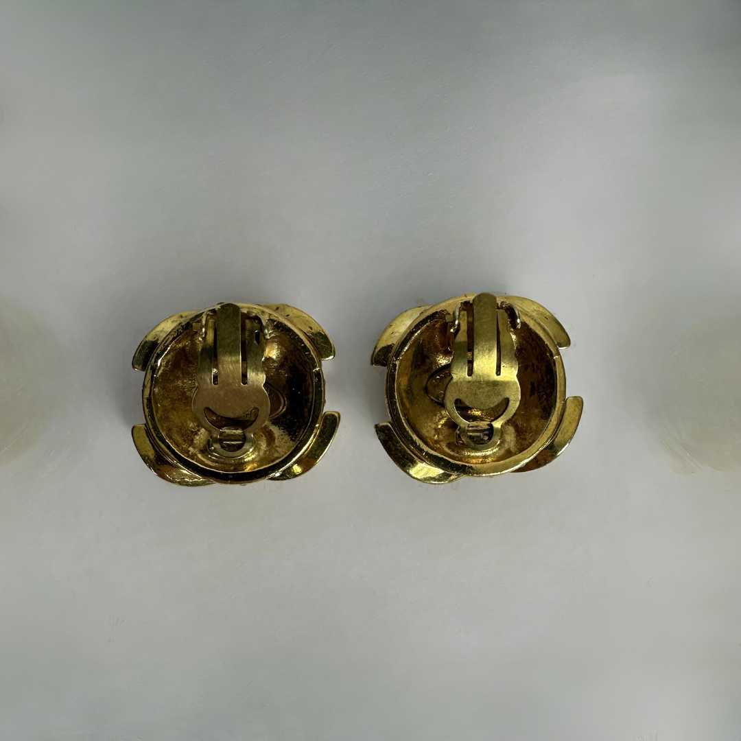 A pair of gold-tone metal clip-on earrings shown from the back on a plain light gray background.