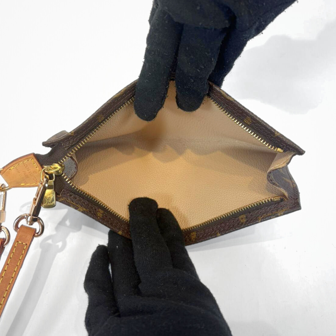 Brown leather handbag with gold accents held open by black-gloved hands on a white background