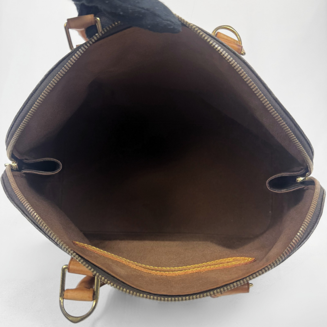 Top-down view of a brown leather handbag interior with a gold-tone zipper, brown fabric lining, and tan leather trim on a white background.
