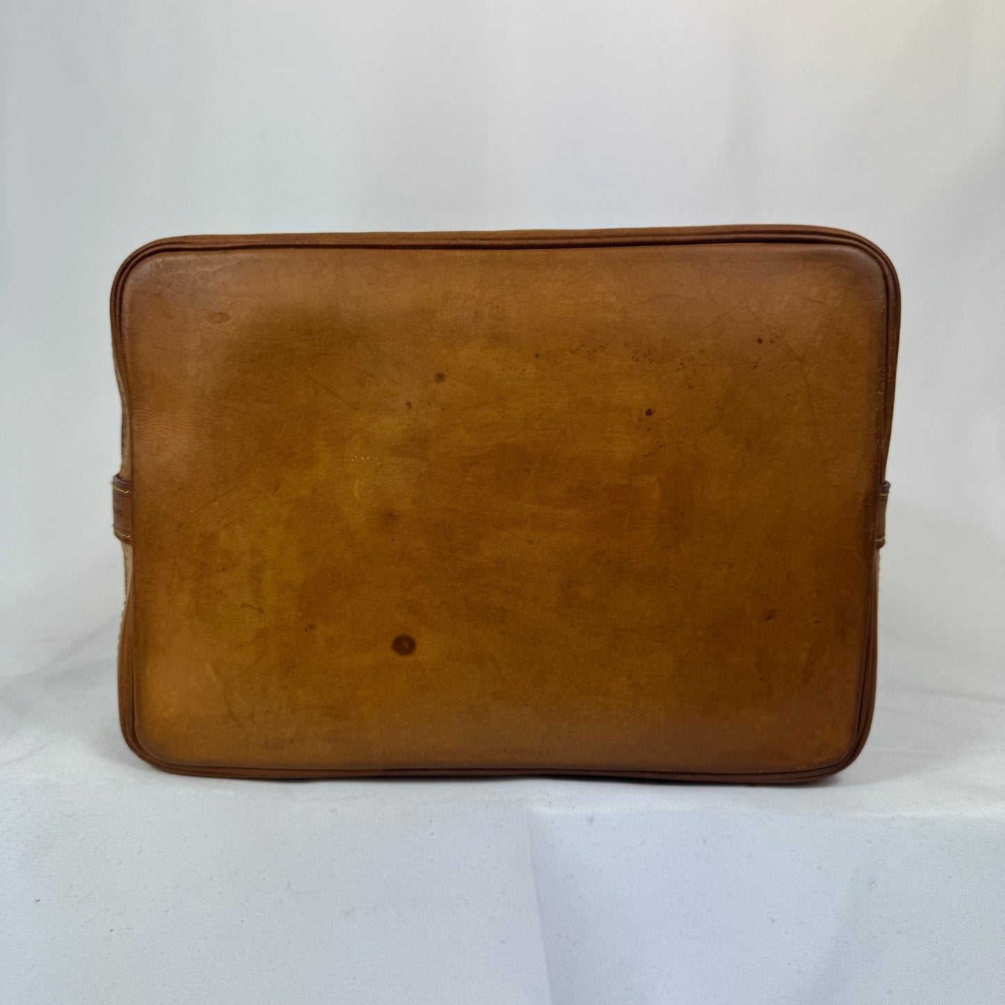 A vintage brown leather laptop sleeve or document holder, showing signs of wear and scuffs, photographed against a white fabric backdrop.