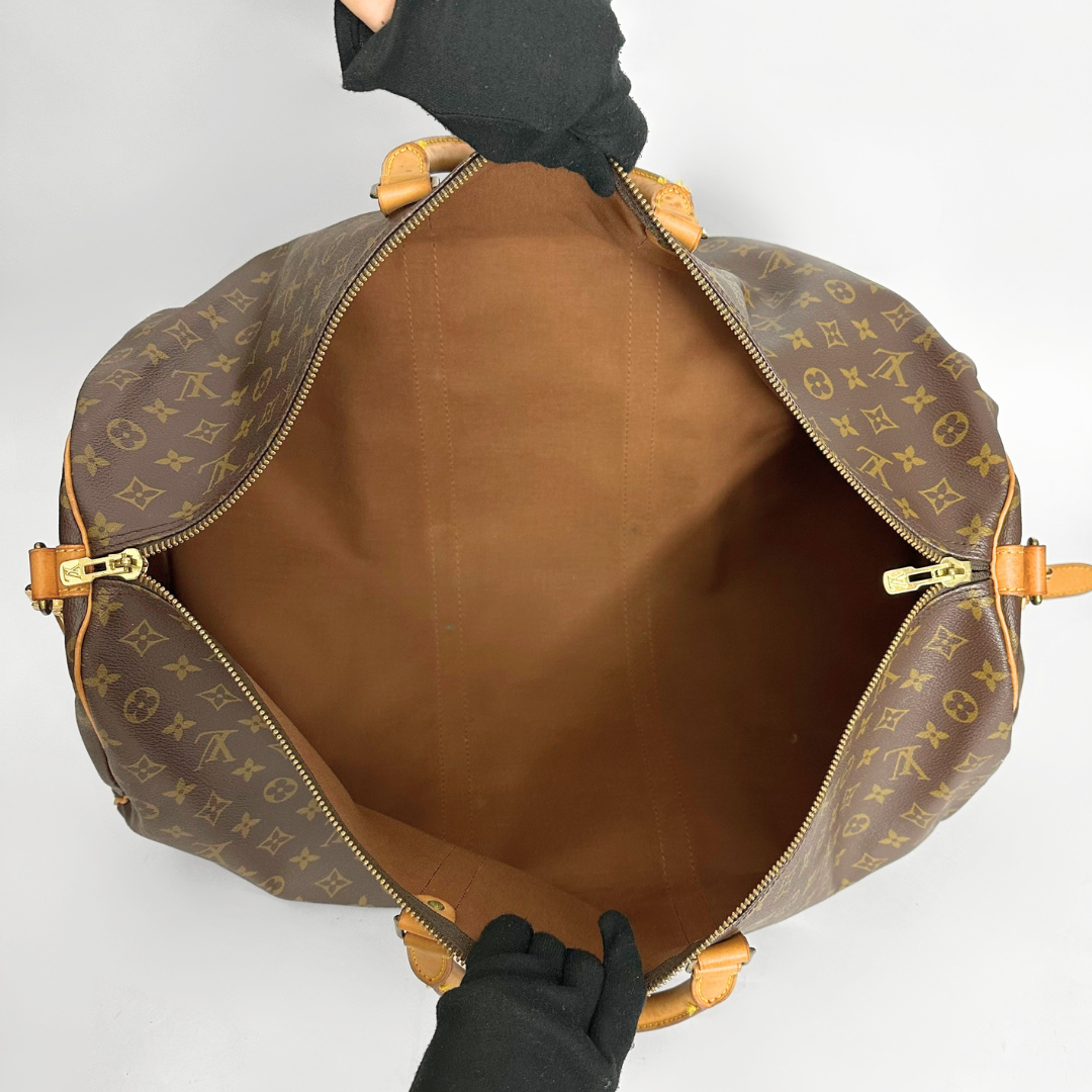 Brown monogrammed bag with gold accents held by a gloved hand on a light gray background