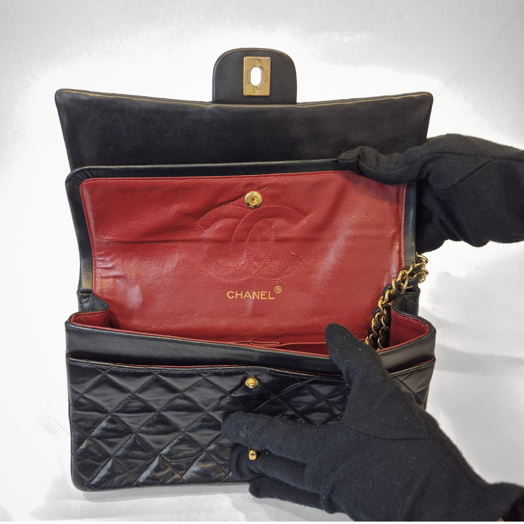 Black quilted handbag with red interior, featuring Chanel logo, held open by a gloved hand.