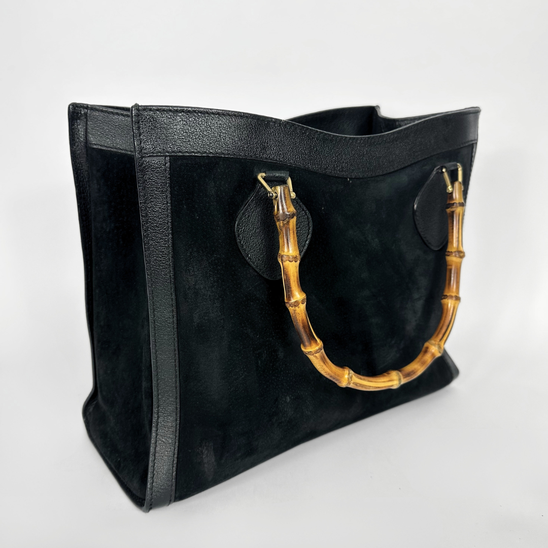Black handbag with gold bamboo handles on a white background