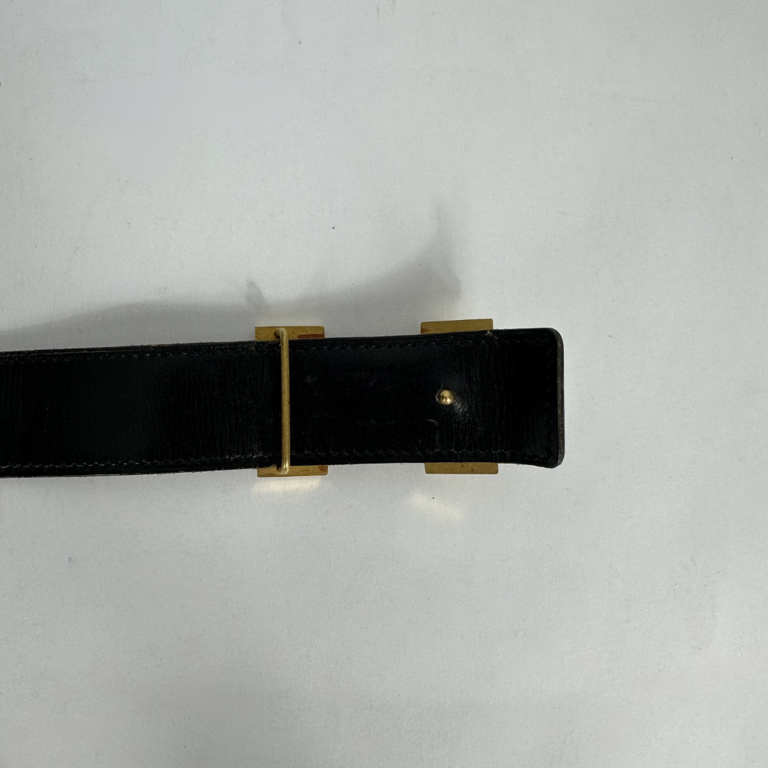 A close-up of a black leather belt with a gold-tone metal buckle, shown against a plain light gray background.
