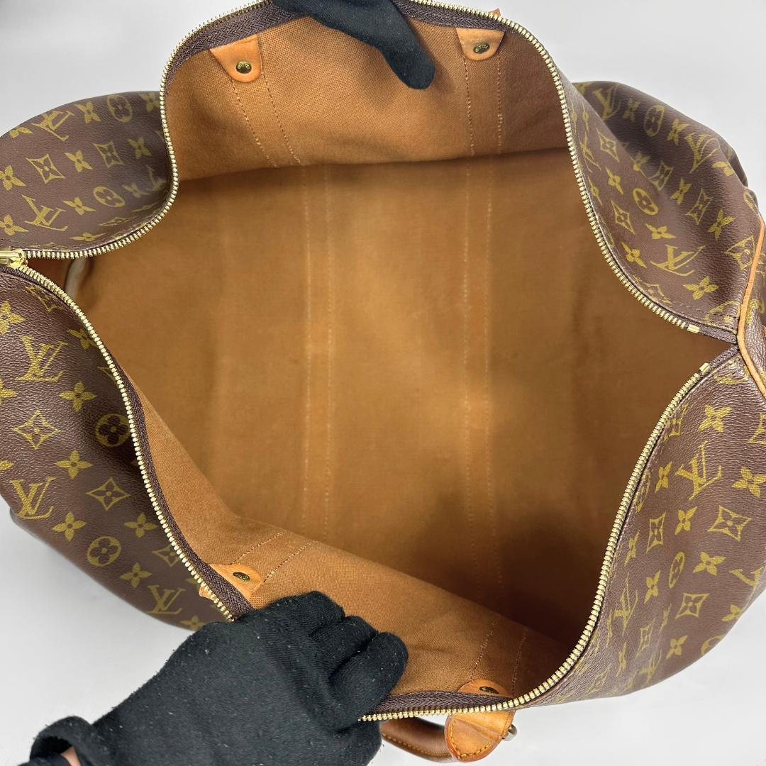 Brown leather bag with gold monogram pattern held open by a gloved hand on a white background
