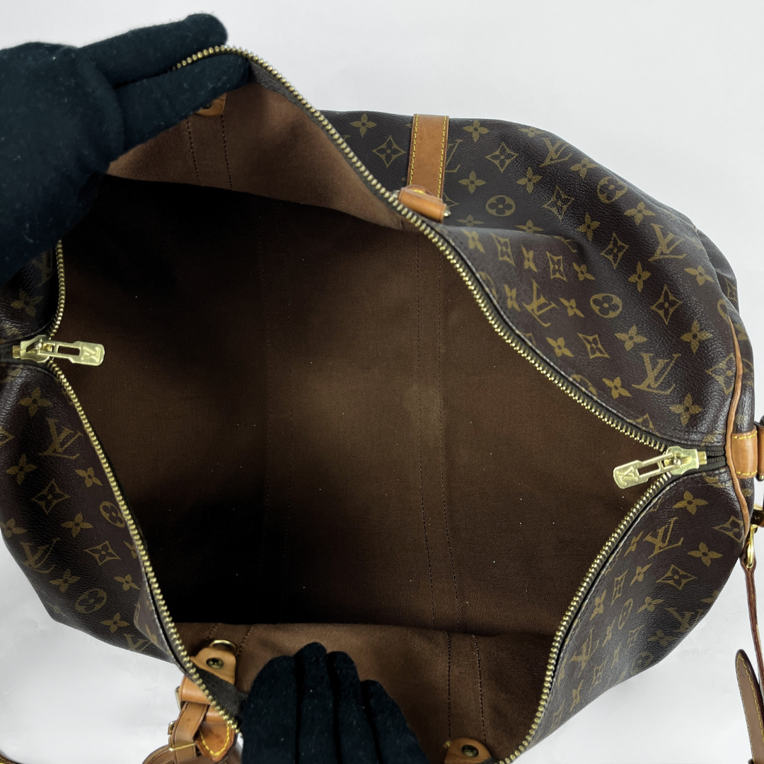 Open Louis Vuitton monogram canvas bag showing the brown interior lining and gold-tone zippers, with gloved hands holding the opening against a white background.