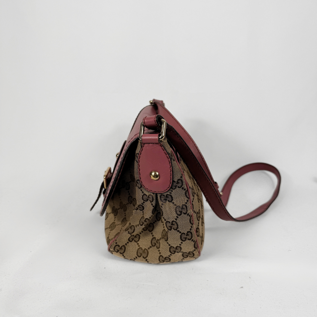 A Gucci crossbody bag in the classic GG Supreme canvas with burgundy leather trim and strap, shown from a side profile view on a white background.