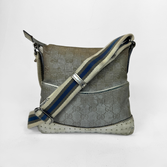 A Gucci GG canvas crossbody bag in metallic silver with a blue and beige striped shoulder strap, silver-tone hardware and a studded base, photographed against a plain white background.