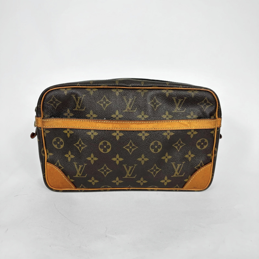 A Louis Vuitton monogram canvas toiletry bag with brown leather trim and corner patches, photographed against a plain light gray background.