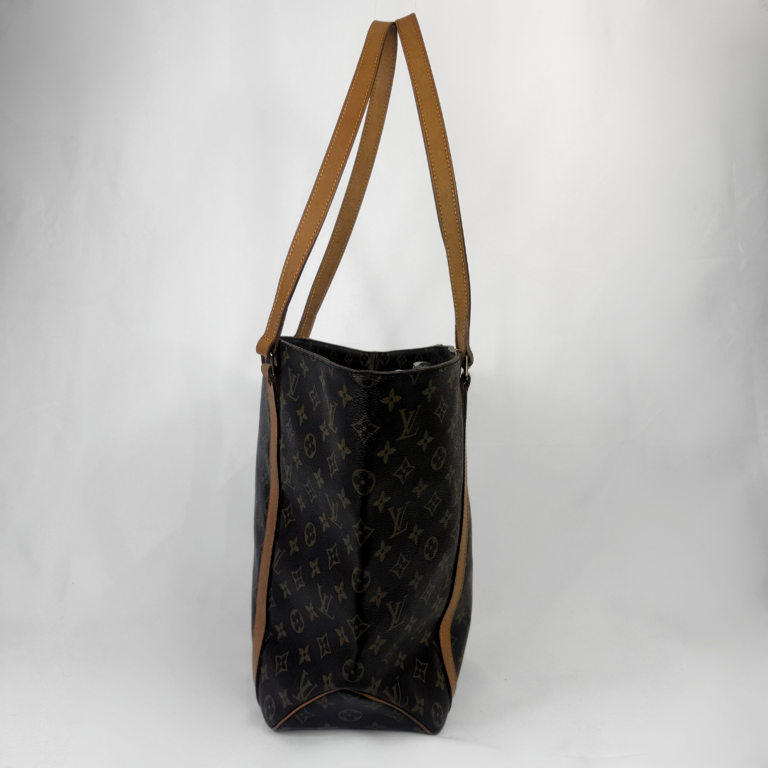 A Louis Vuitton monogram tote bag in dark brown coated canvas with tan leather shoulder straps, shown against a light gray studio background.