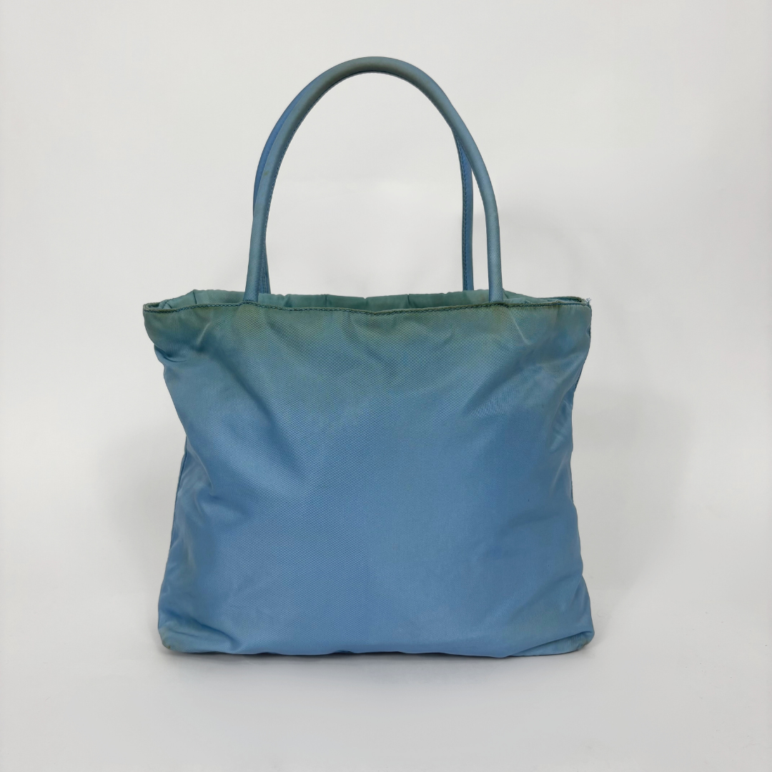 Prada light blue nylon tote bag with matching top handles and the signature enamel triangle logo.