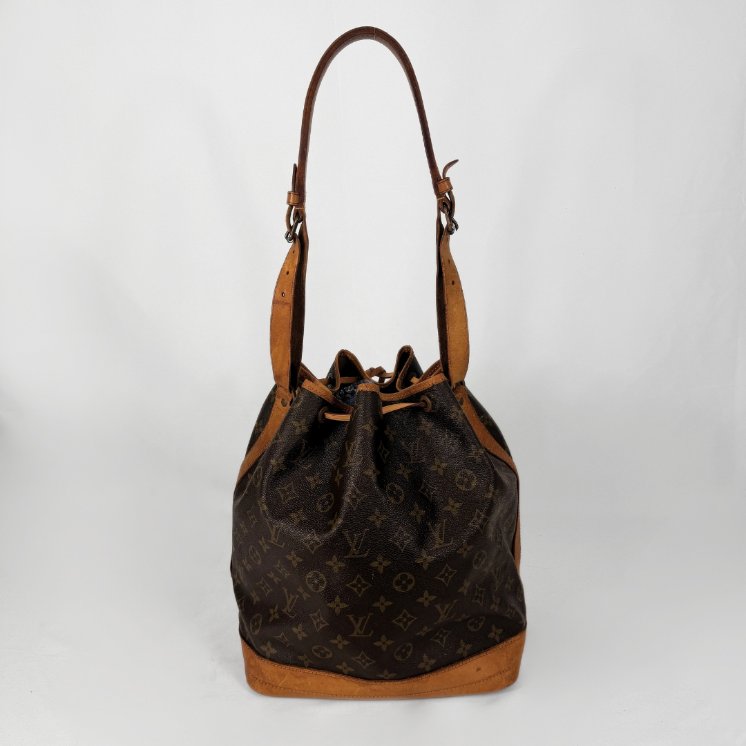 A vintage Louis Vuitton monogram canvas bucket bag with tan leather trim and a single shoulder strap, photographed against a neutral light gray background.