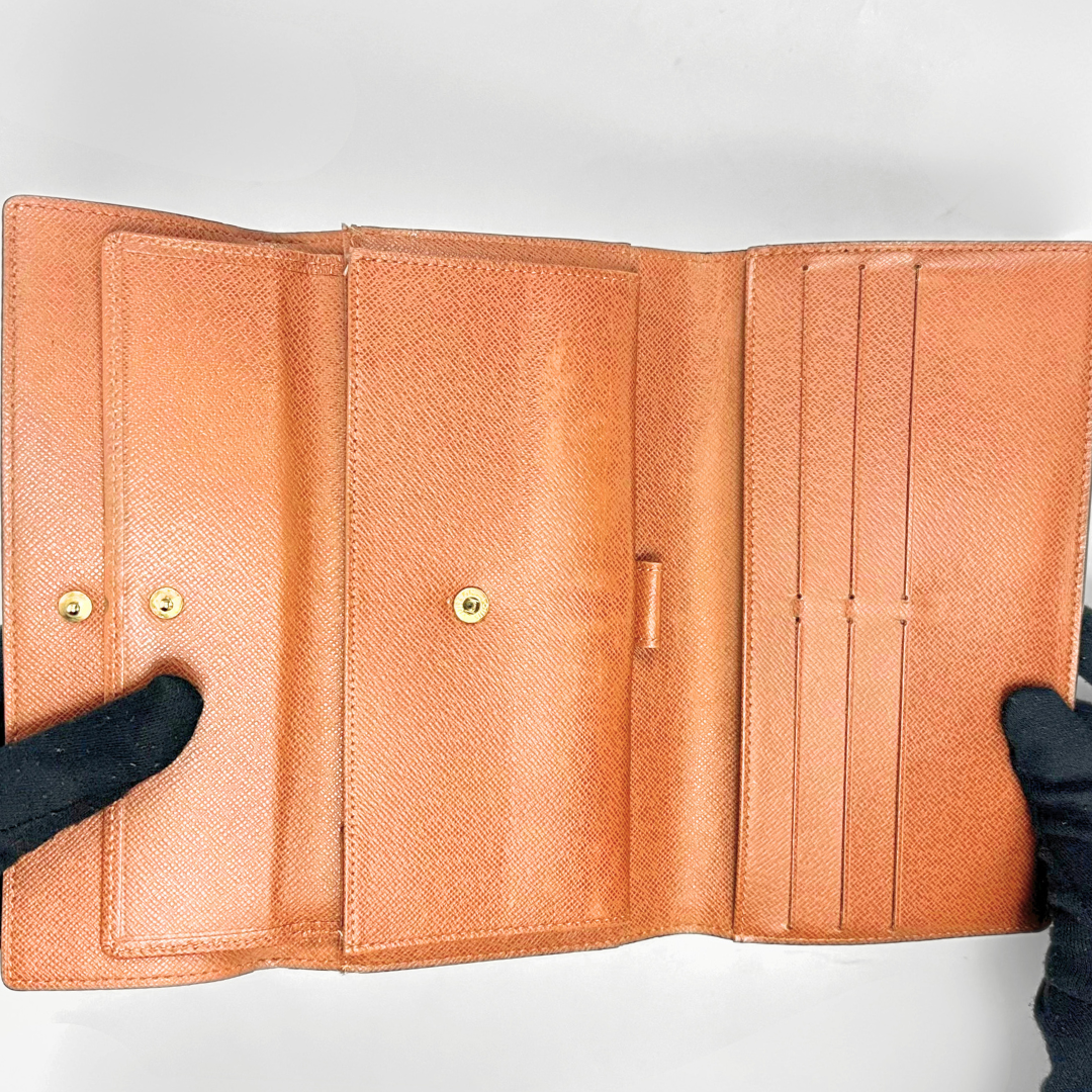 Brown leather wallet held open by black-gloved hands on a white background