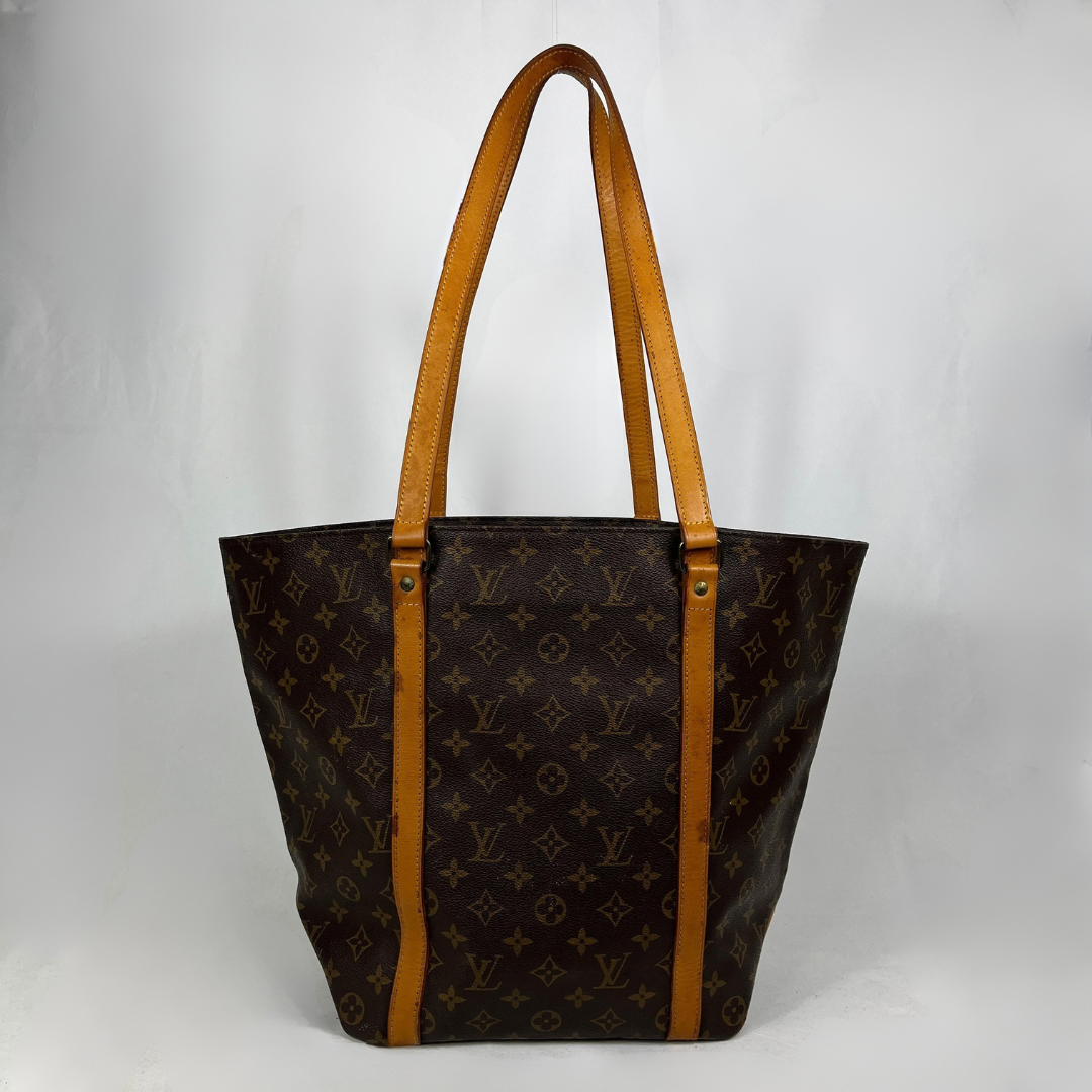 A Louis Vuitton monogram canvas tote bag with tan leather shoulder straps and trim, shown against a light gray background.