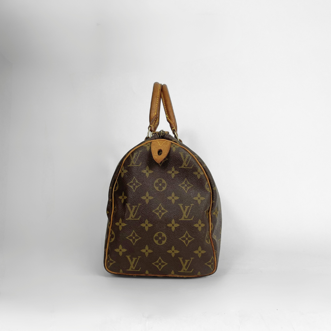 A Louis Vuitton monogram Speedy bag in brown coated canvas with tan leather handles and trim, photographed against a light gray studio background.