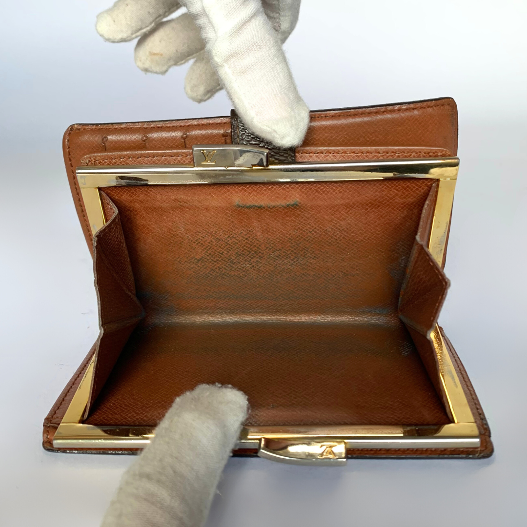A vintage brown leather clutch purse with gold-tone metal hardware, shown open with a white-gloved hand adjusting the clasp. The interior is lined in matching brown textured leather.