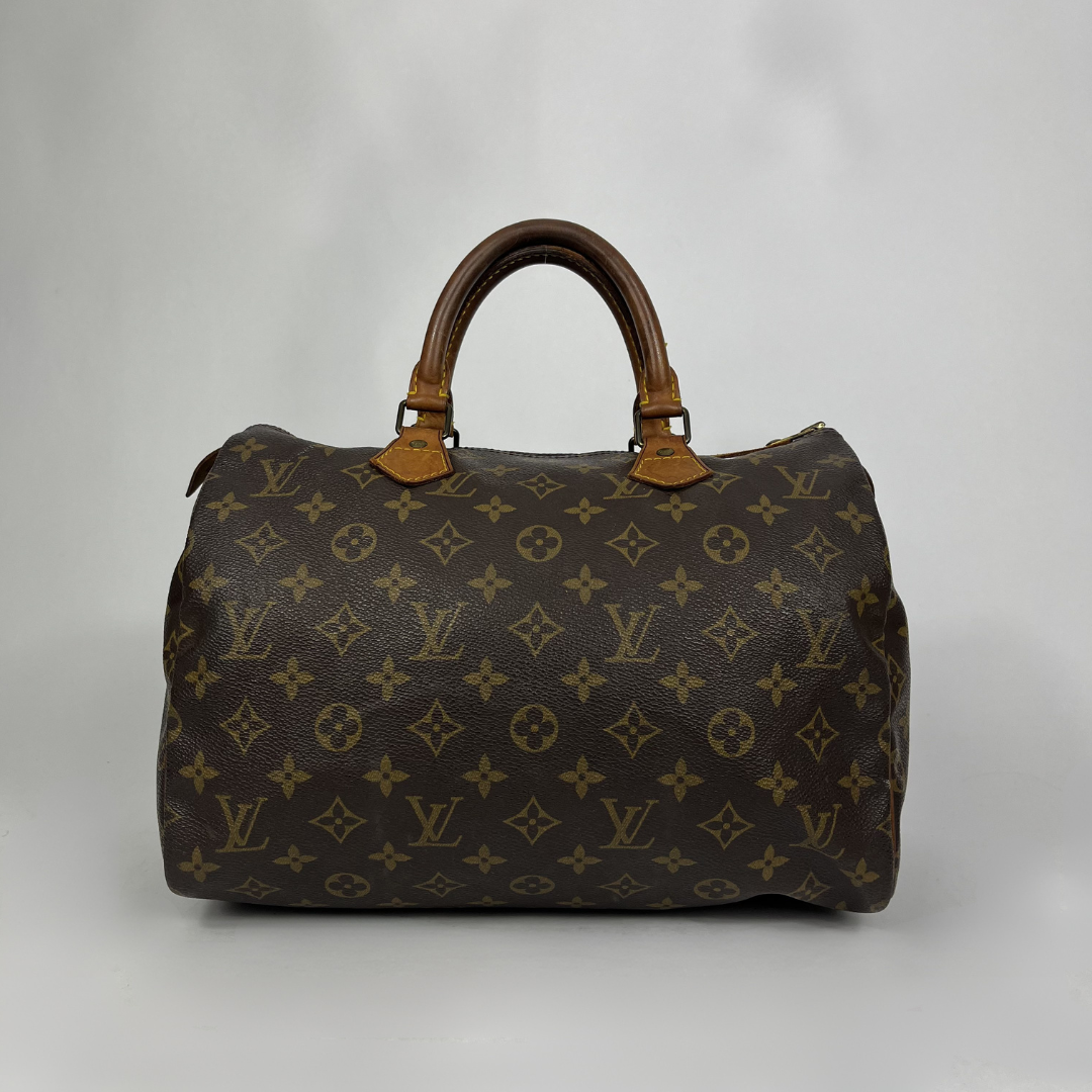 A classic Louis Vuitton monogram Speedy bag in dark brown coated canvas with tan leather handles, set against a neutral gray studio background.