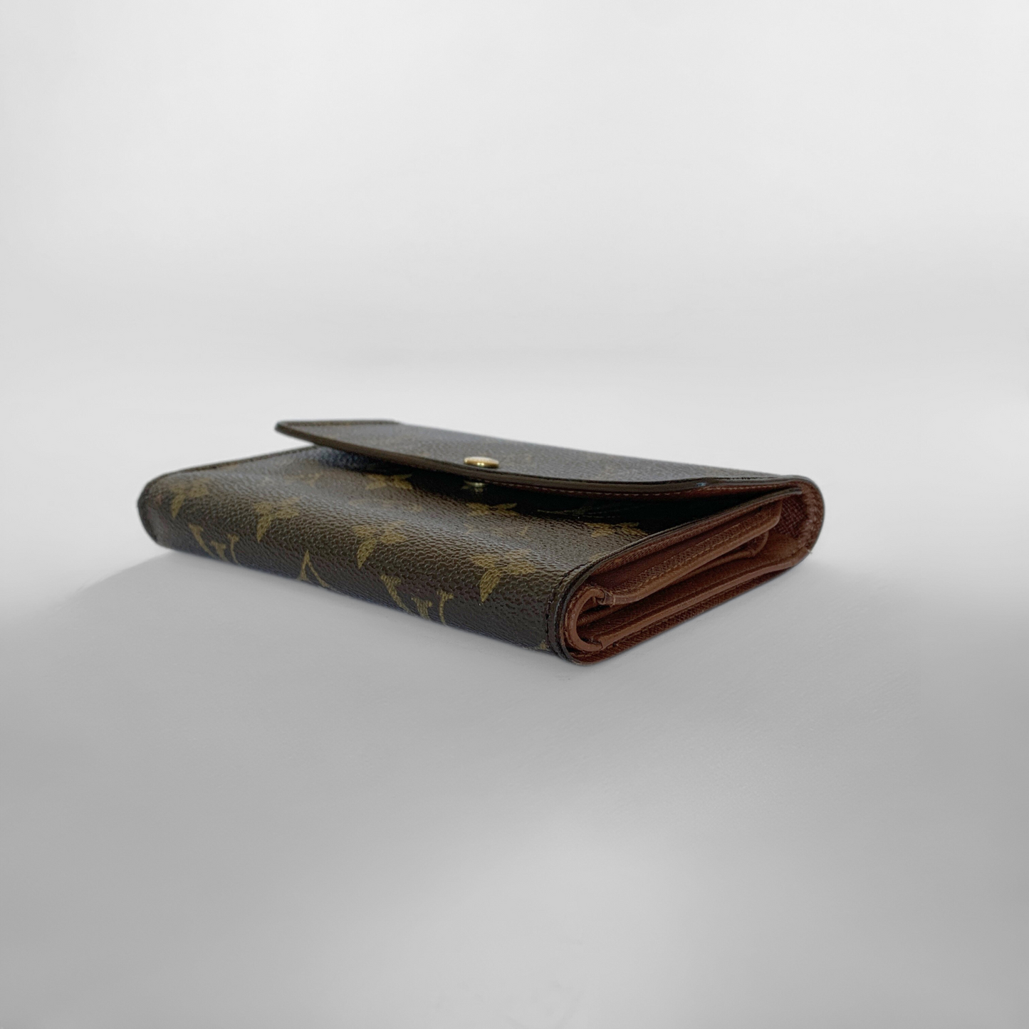 Folded brown leather wallet with gold monogram pattern on a light gray background