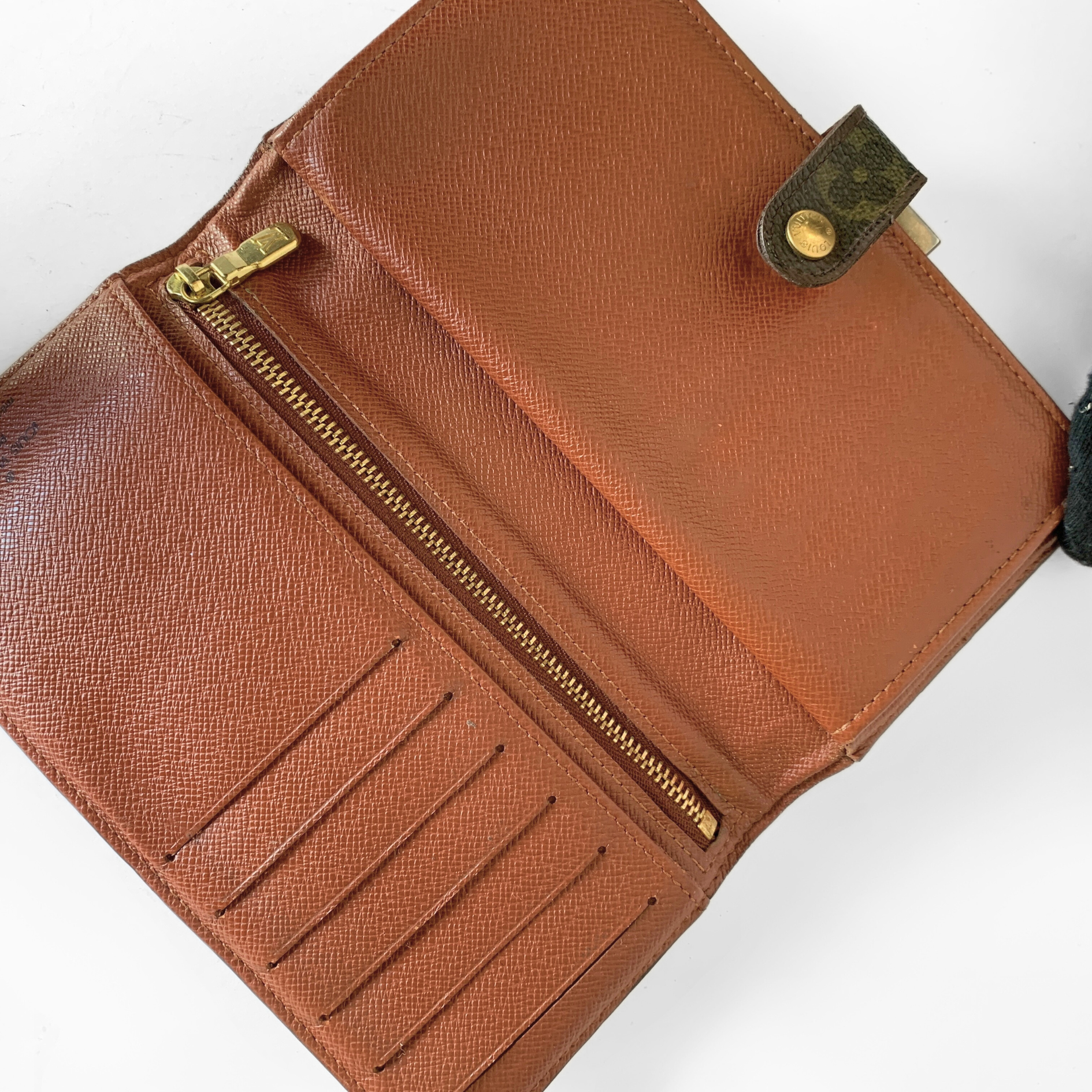 An open brown textured leather wallet with gold-tone zippers, card slots, and a small dark brown leather accent tab with a gold snap, photographed on a white background.