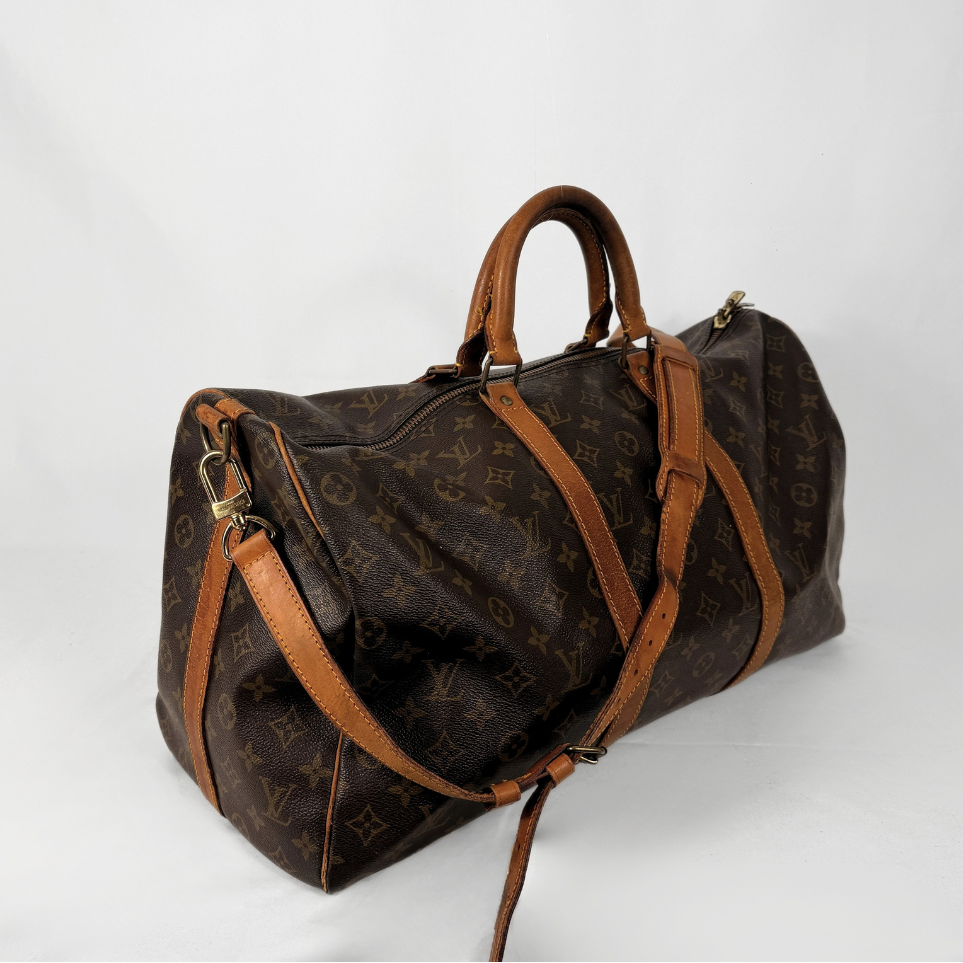 A Louis Vuitton monogram canvas duffel bag with brown leather handles and shoulder straps, photographed on a white studio background.