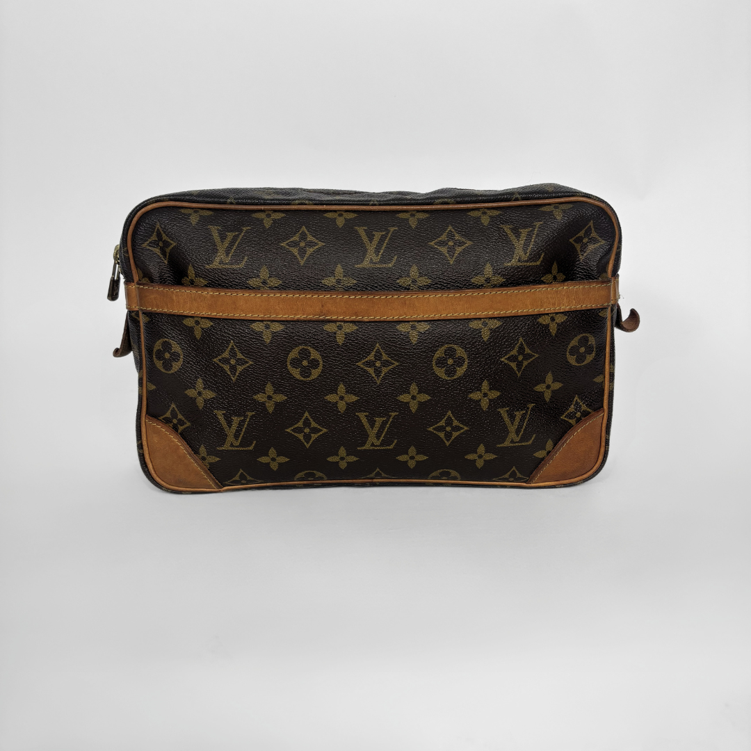 A Louis Vuitton monogram canvas pouch bag with brown leather trim and corner protectors, photographed against a neutral light gray background.