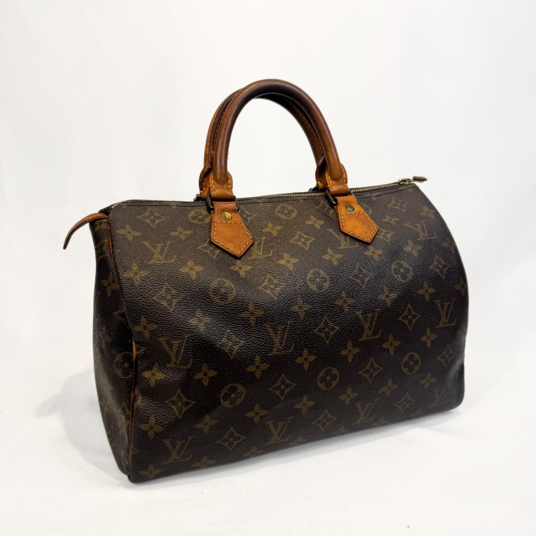 A Louis Vuitton monogram canvas Speedy handbag in dark brown with tan leather handles and trim, photographed against a light gray studio background.