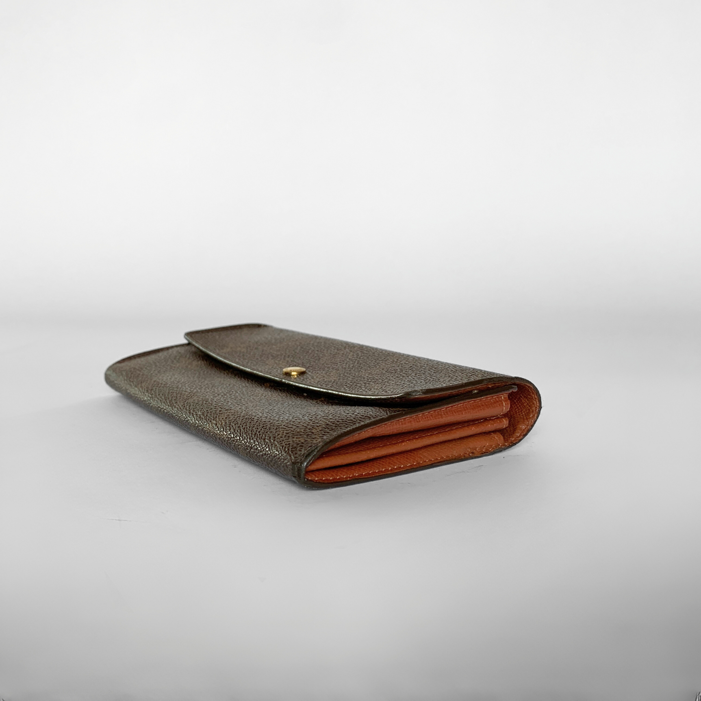 A brown monogrammed leather wallet with a gold snap button and a contrasting orange-brown interior lining, shown on a light gray background.