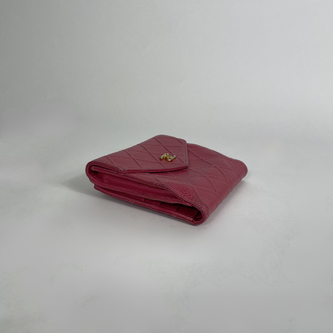 A folded quilted leather wallet in a deep magenta pink, featuring a small gold-tone metal logo clasp on the front flap, set against a plain light gray background.