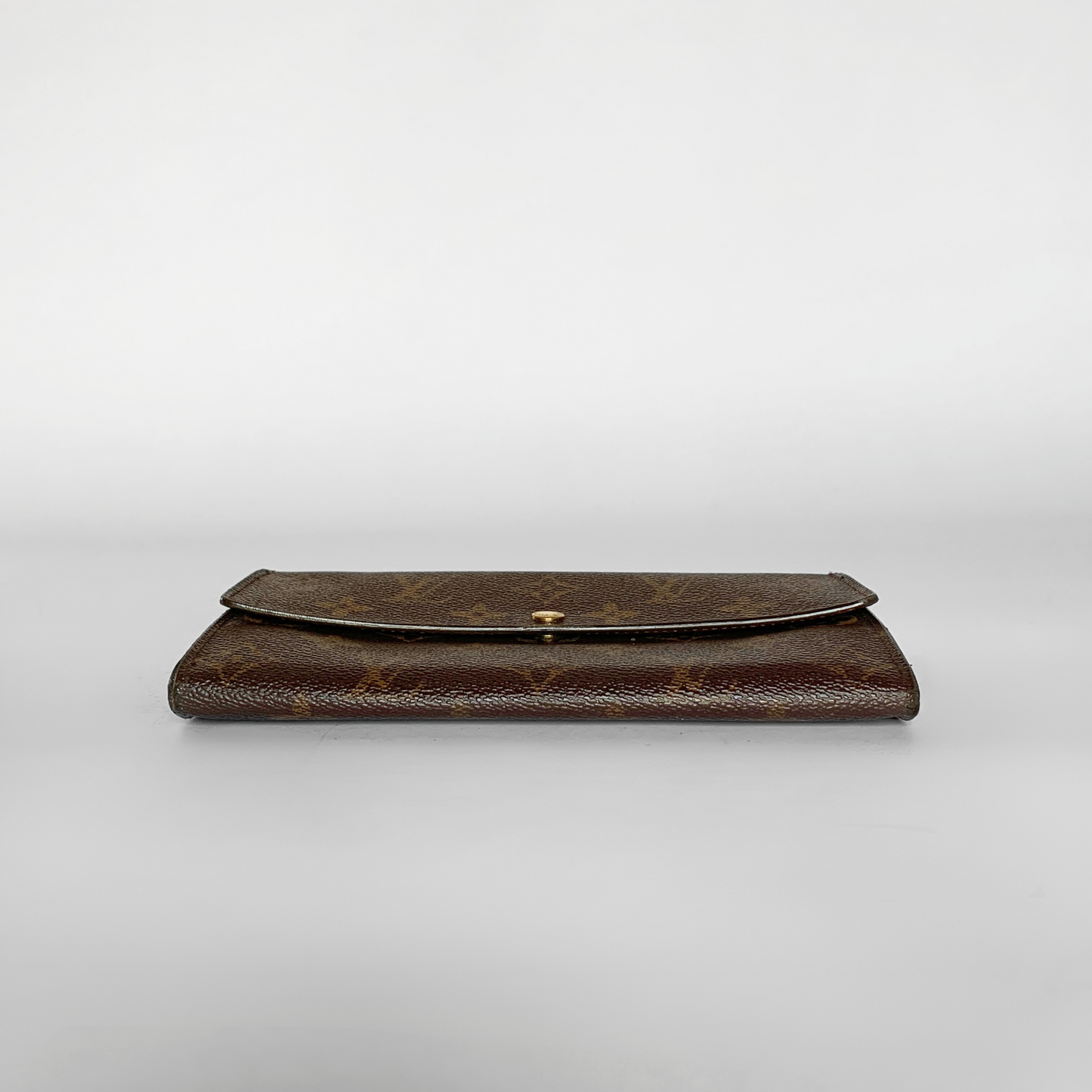 A brown monogram wallet with a flap closure and a small gold clasp, photographed against a neutral light gray background.