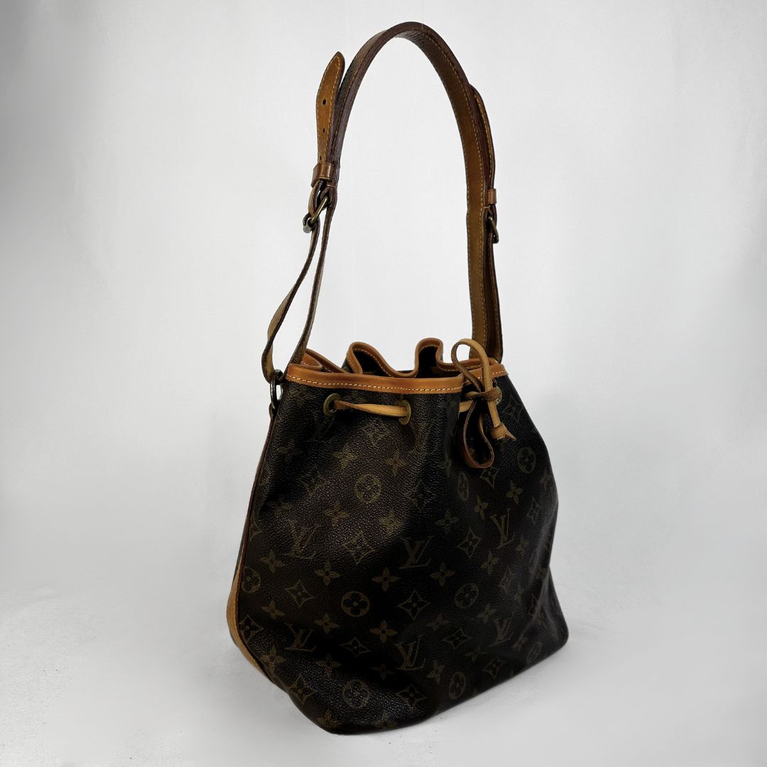 Louis Vuitton monogram canvas bucket bag with tan leather trim and shoulder strap, shown on a light gray background.