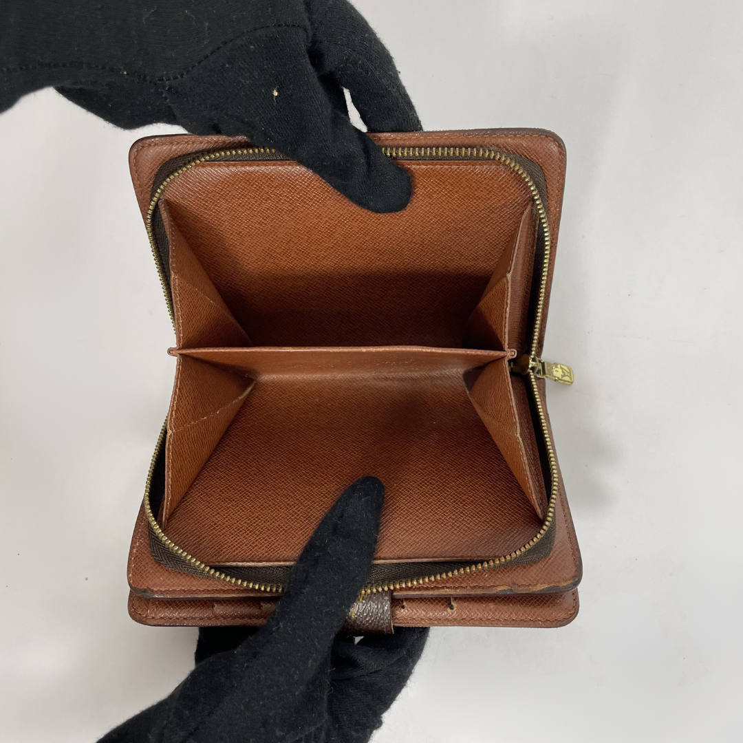 A brown leather zip-around wallet shown open, held by black-gloved hands against a plain light background.