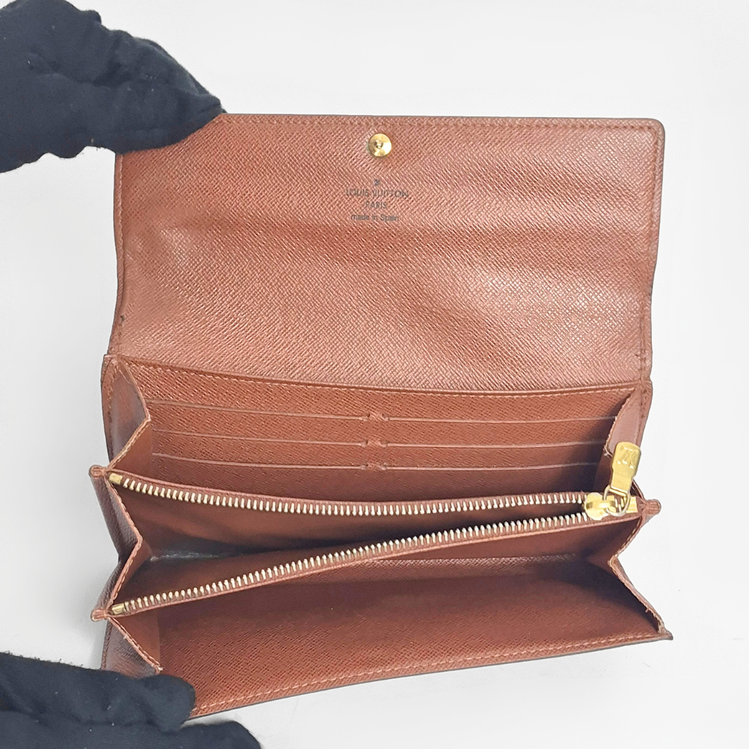 Brown leather wallet with gold accents held open by a gloved hand on a white background