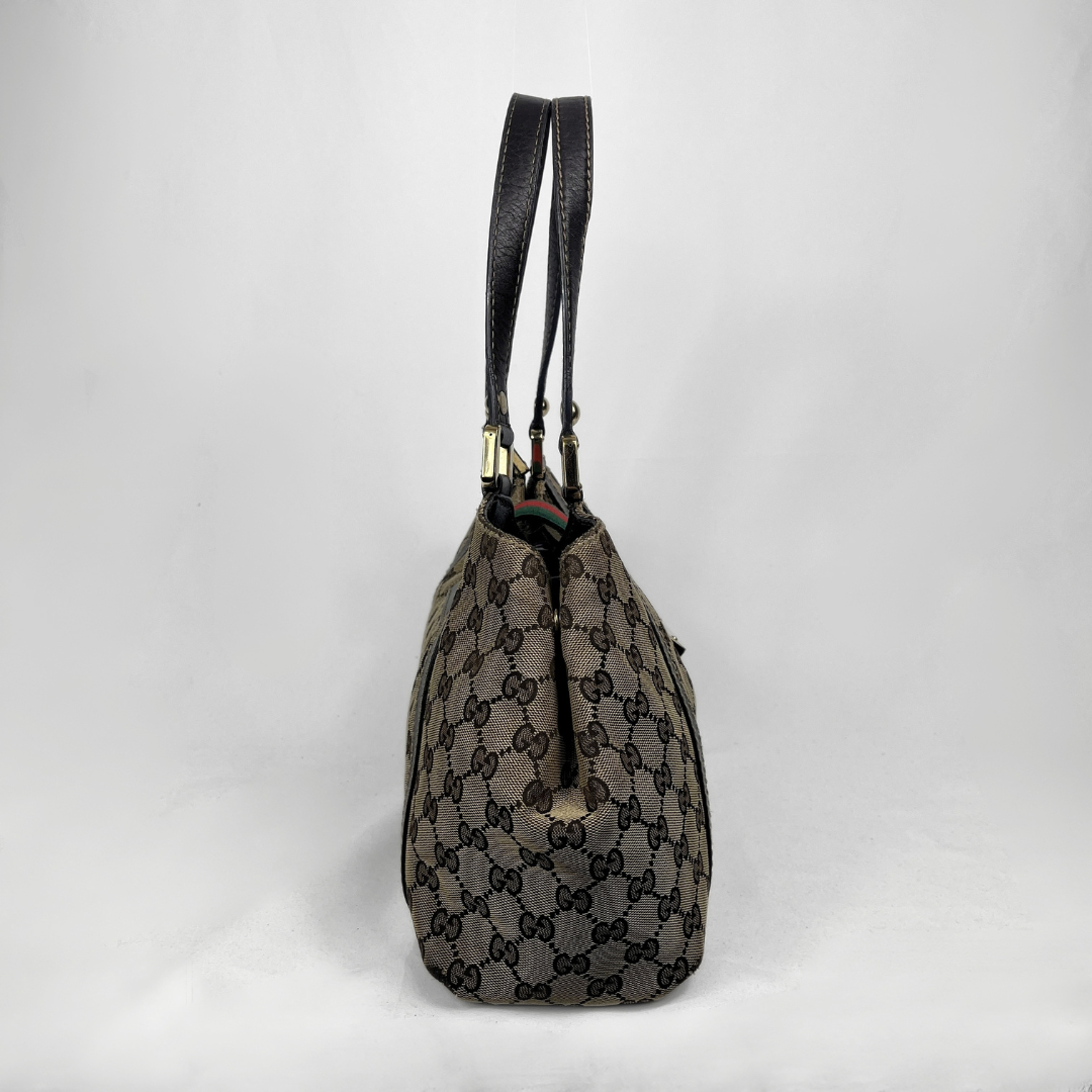 A vintage Gucci monogram canvas shoulder bag with black leather straps, shown from the back against a light gray studio background.