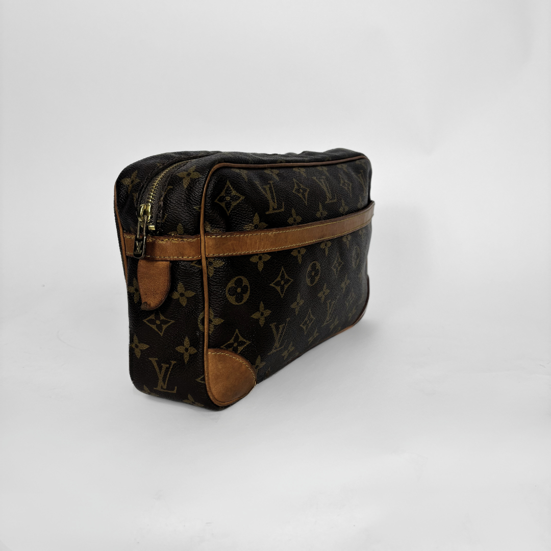 A Louis Vuitton monogram canvas toiletry bag with brown leather trim and a gold-tone zipper, photographed on a light gray studio background.