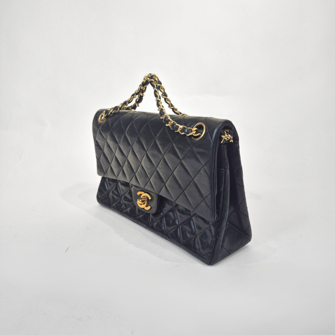 Black quilted handbag with gold chain and clasp on a white background