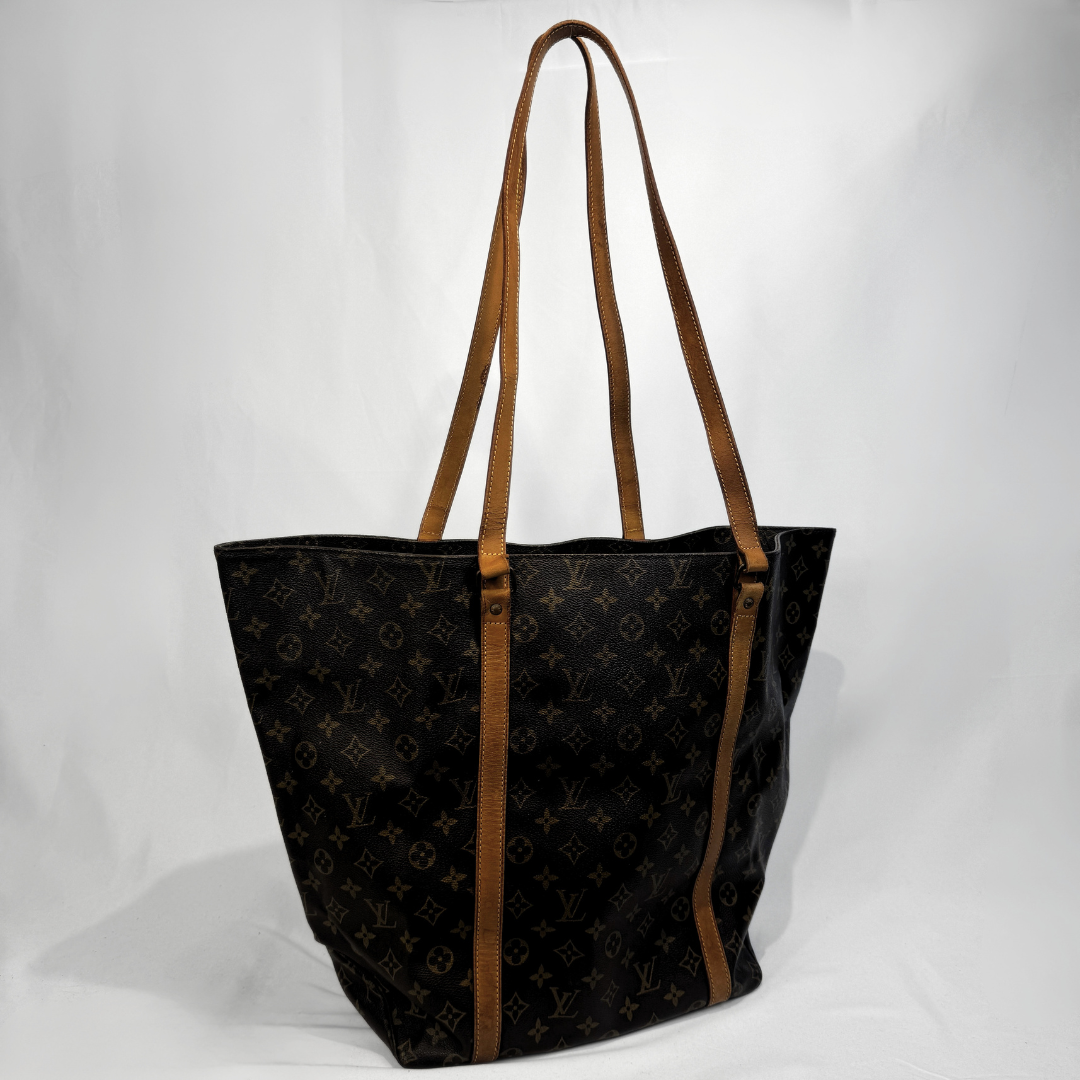 A Louis Vuitton monogram canvas tote bag with brown leather shoulder straps, photographed against a white studio backdrop.