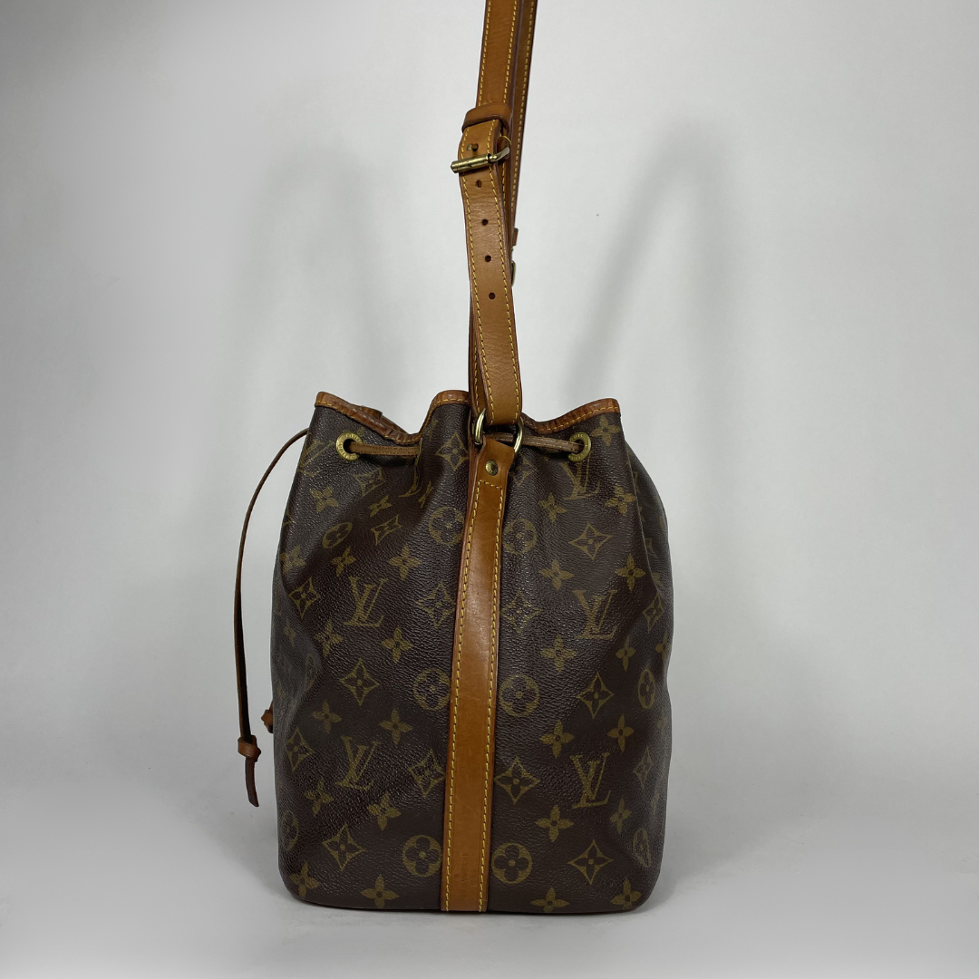 Louis Vuitton monogram canvas bucket bag with tan leather trim and shoulder strap, shown against a neutral light gray background.