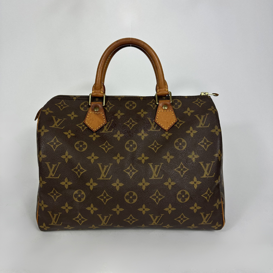 A Louis Vuitton monogram canvas Speedy handbag with brown leather handles and gold-tone hardware, photographed against a neutral light gray background.