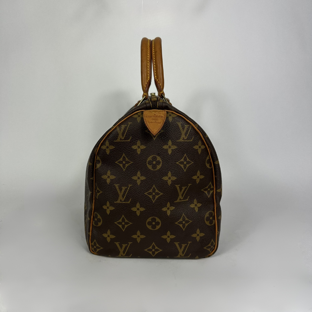 A Louis Vuitton monogram canvas Speedy bag with tan leather handles and trim, photographed against a plain light gray background.