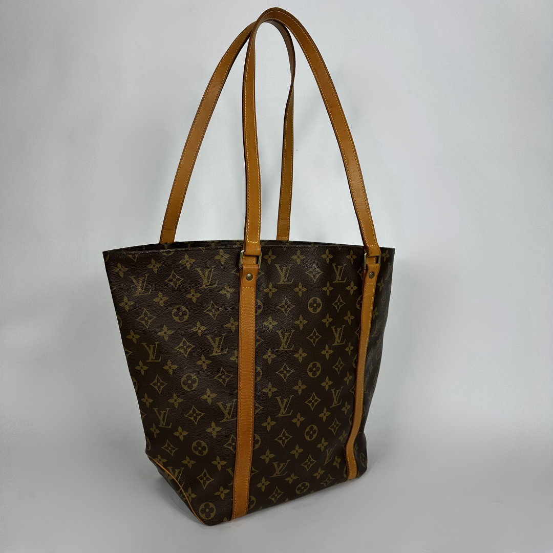 Louis Vuitton monogram canvas tote bag with tan leather shoulder straps and trim, shown on a light gray background.