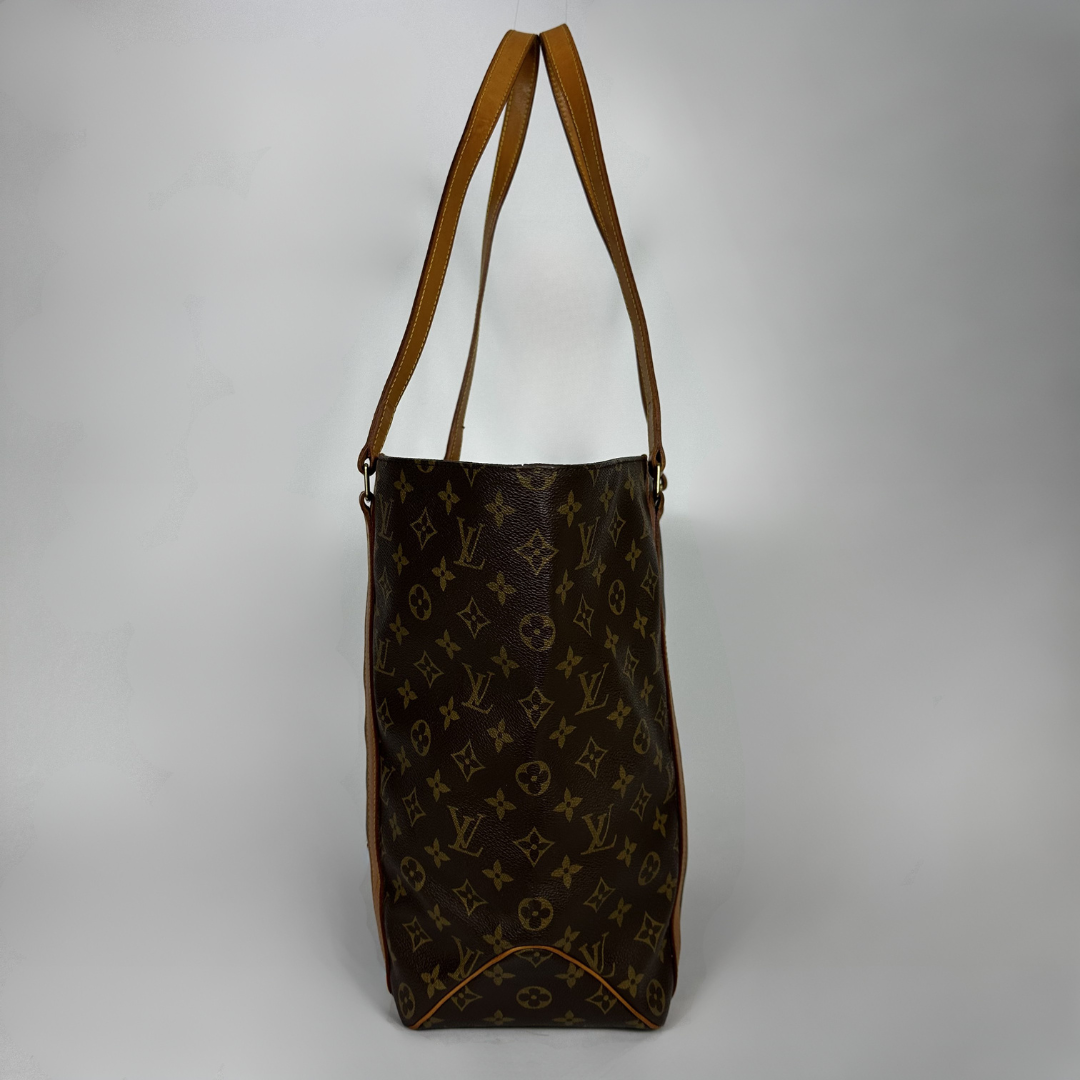 A Louis Vuitton monogram tote bag in dark brown coated canvas with tan leather shoulder straps, shown against a neutral gray background.