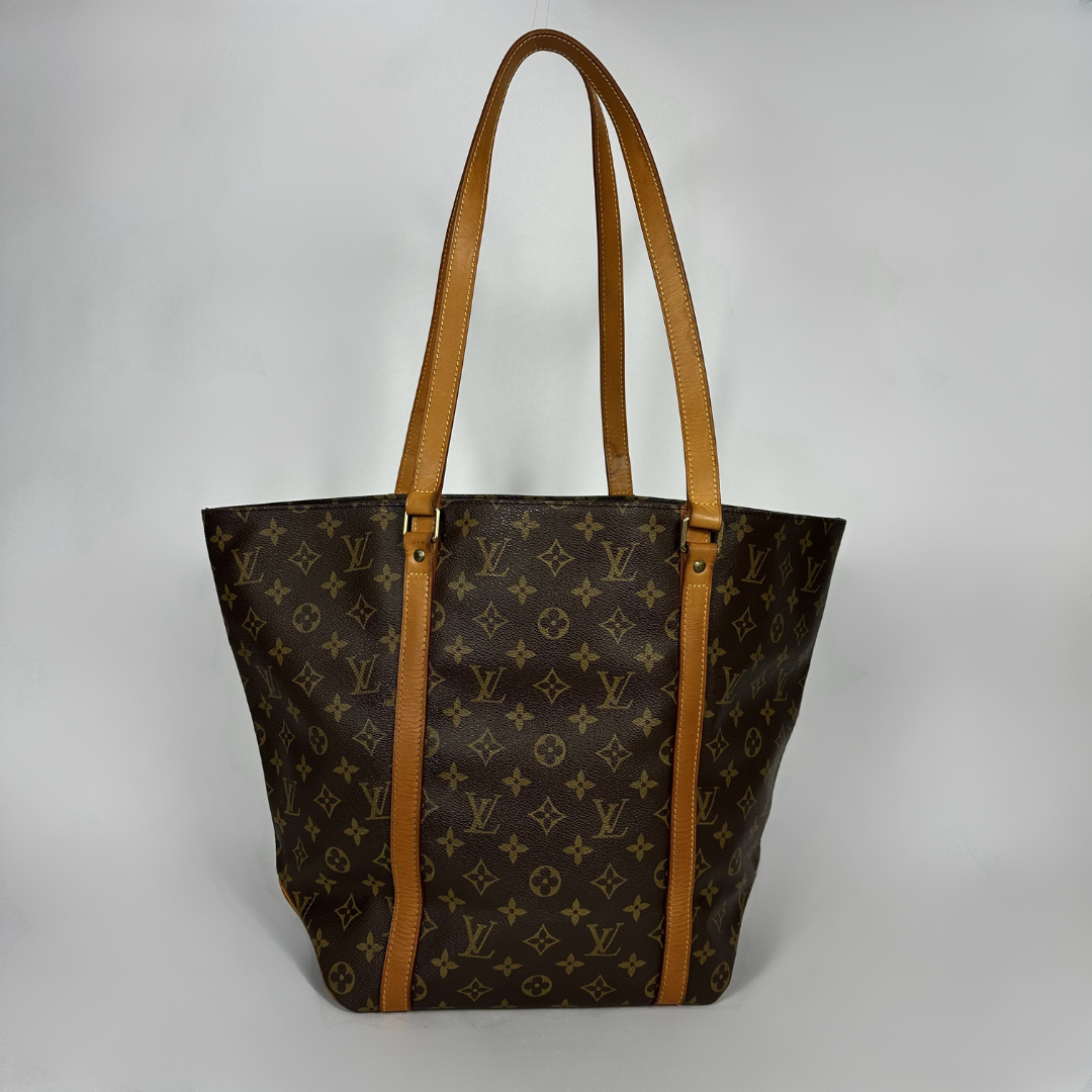 A Louis Vuitton monogram canvas tote bag with tan leather shoulder straps, photographed against a neutral light gray background.