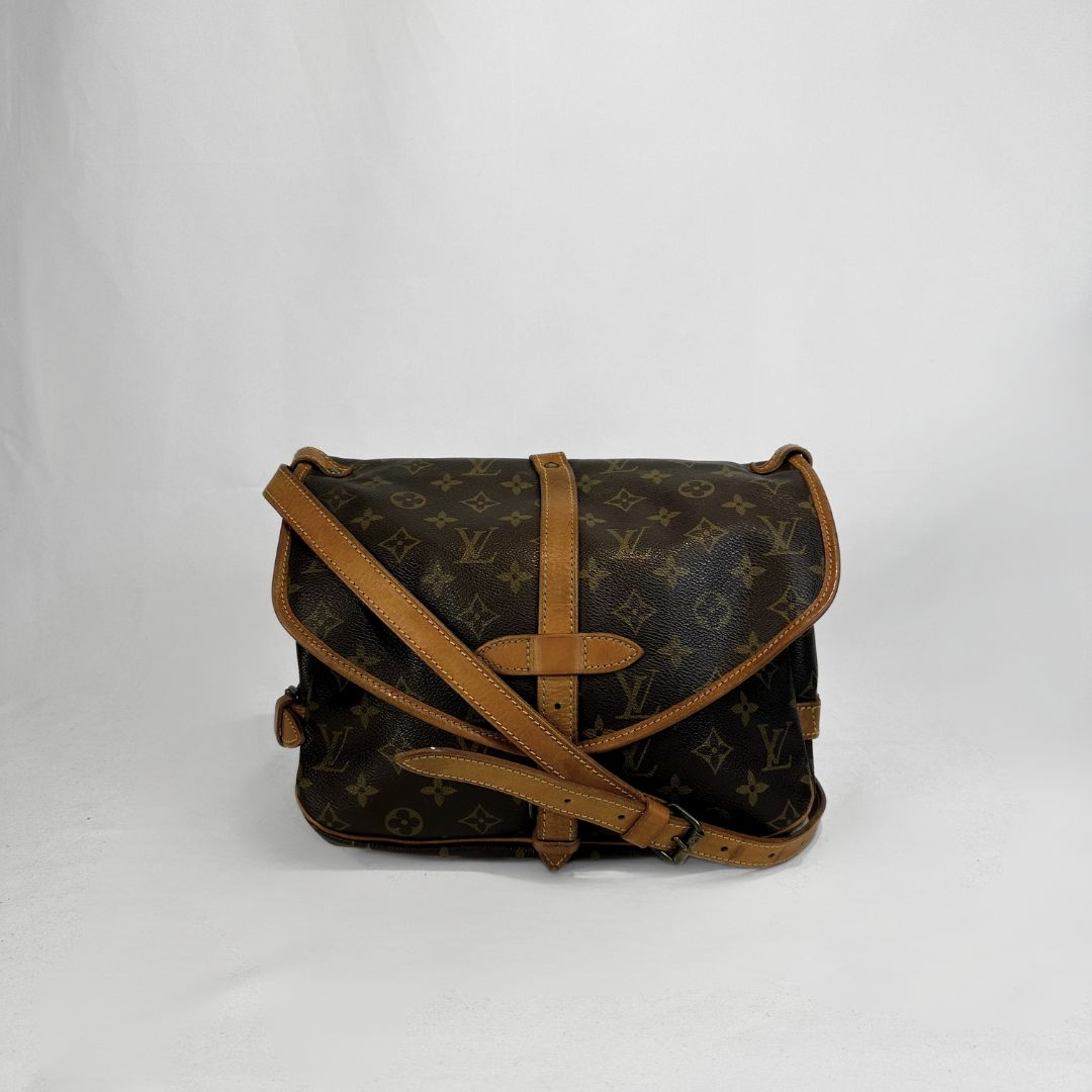 A Louis Vuitton monogram canvas shoulder bag with tan leather trim and strap, photographed against a plain light gray background.