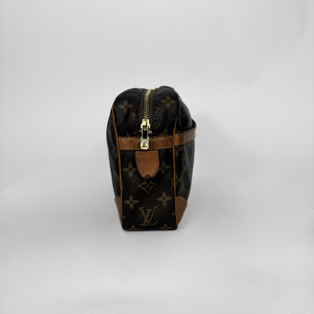 Louis Vuitton monogram canvas toiletry bag with brown leather trim and gold-tone zipper, photographed on a light gray studio background.