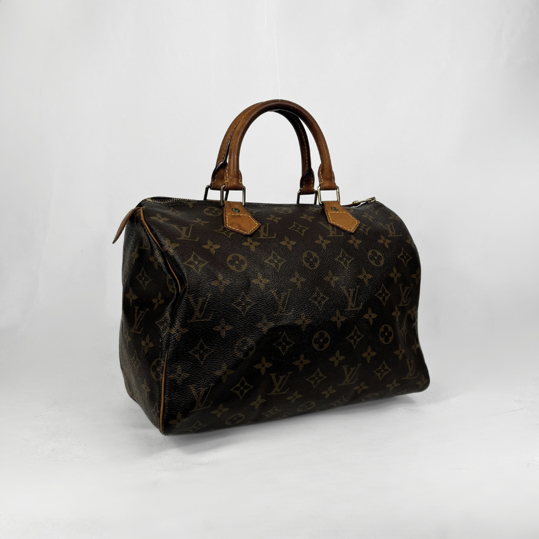 A Louis Vuitton monogram canvas Speedy handbag in dark brown with tan leather handles and trim, photographed against a light gray studio background.